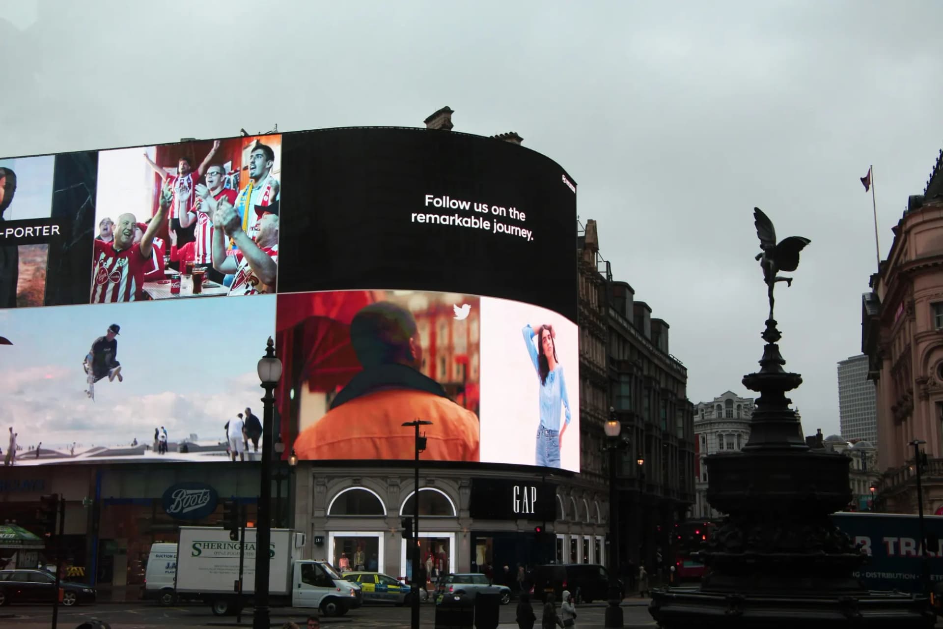 Curved digital billboards showing ads above shops at Piccadilly Circus, London, on an overcast day